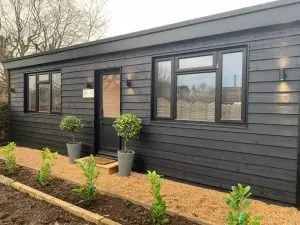 A picture of the clinic taken from outside. it shows the doors and two bay trees either side of the front door. The cabin is black